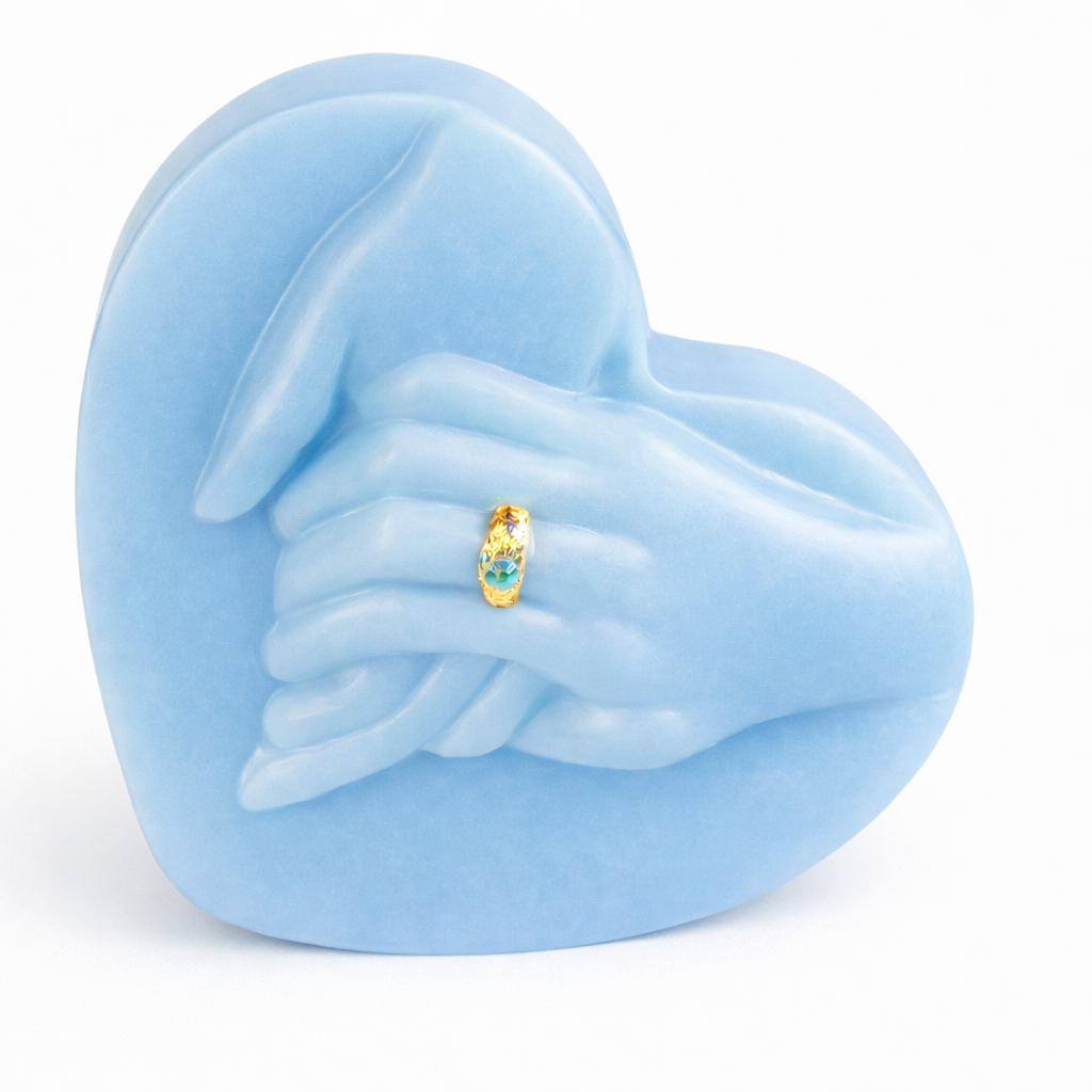 Vela escultórica en forma de corazón con manos entrelazadas color azul cielo, elaborada en cera natural de acabado satinado, diseño artístico contemporáneo con anillo dorado decorativo, pieza exclusiva para decoración de interiores elegantes y regalos de lujo.