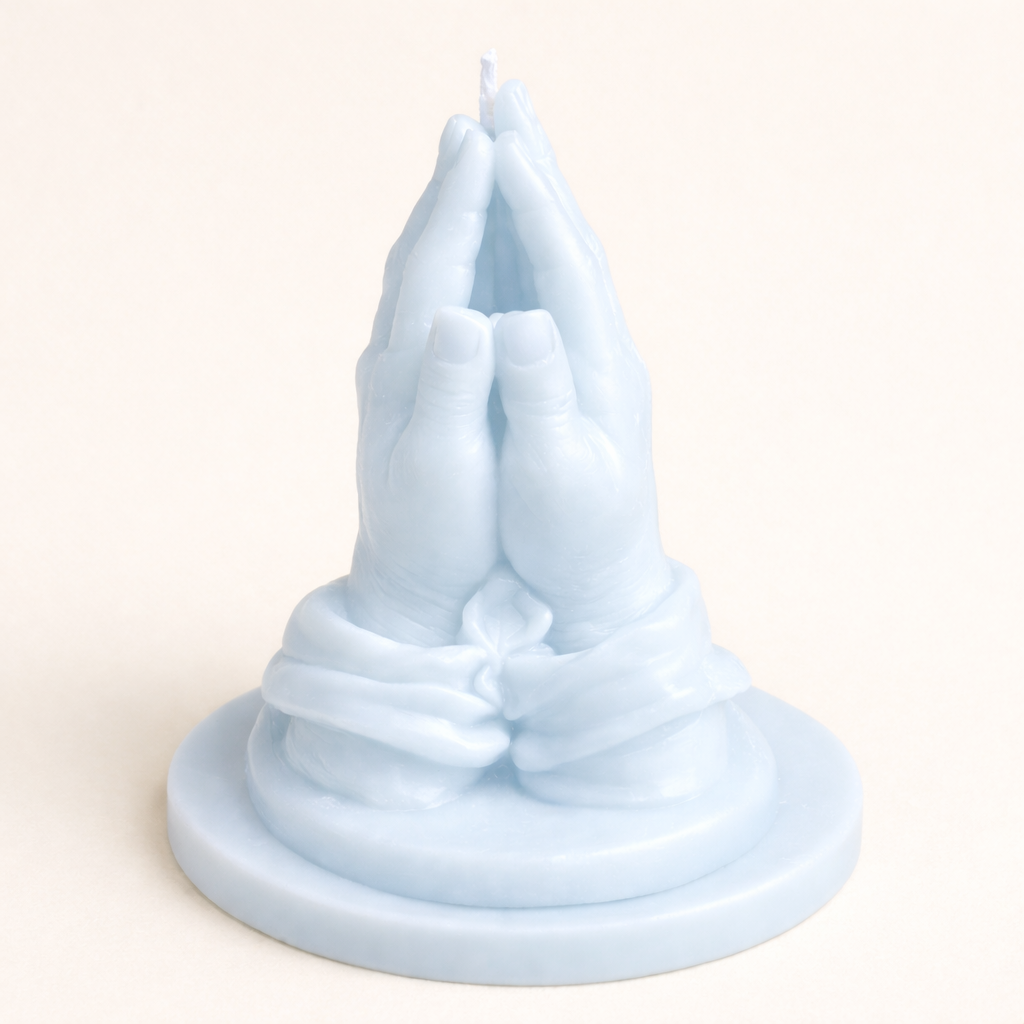 Vela decorativa en forma de manos en oración color azul pastel, elaborada en cera natural con acabado satinado, diseño escultórico minimalista sobre base circular, pieza artística elegante para decoración de interiores de lujo.
