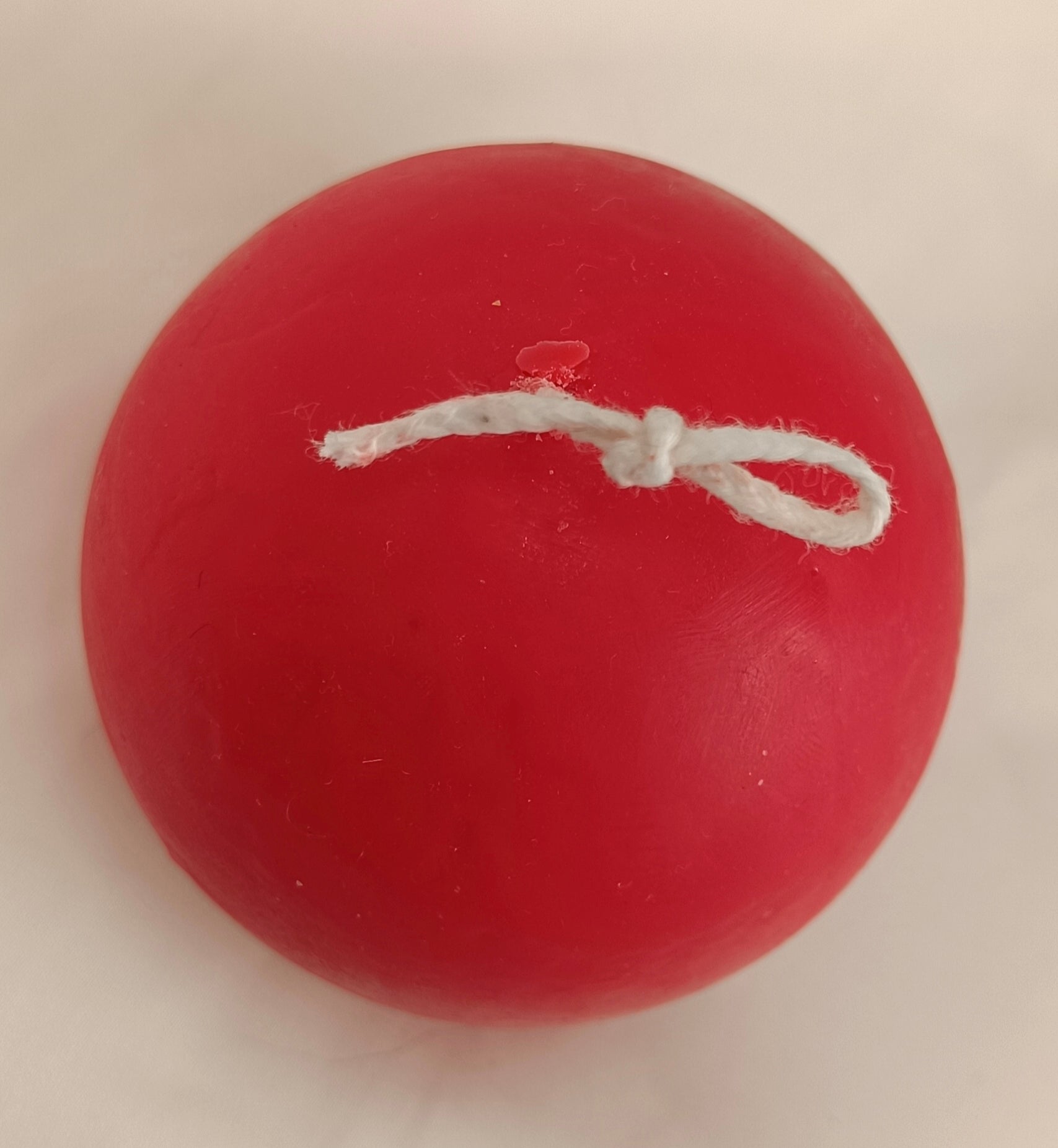 Vela artesanal Bola de Navidad roja con mecha anudada para colgar, hecha a mano con cera natural.