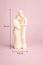 Vela artística en forma de pareja abrazada con diseño contemporáneo, 10 cm de altura y 4,5 cm de ancho, fabricada en cera natural, fotografía de producto premium con fondo rosa suave.