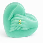 Vela decorativa corazón con manos unidas color verde esmeralda pastel, fabricada en cera natural premium, diseño escultórico moderno con detalle de anillo dorado, objeto artístico sofisticado para decoración boutique y espacios de alto nivel.