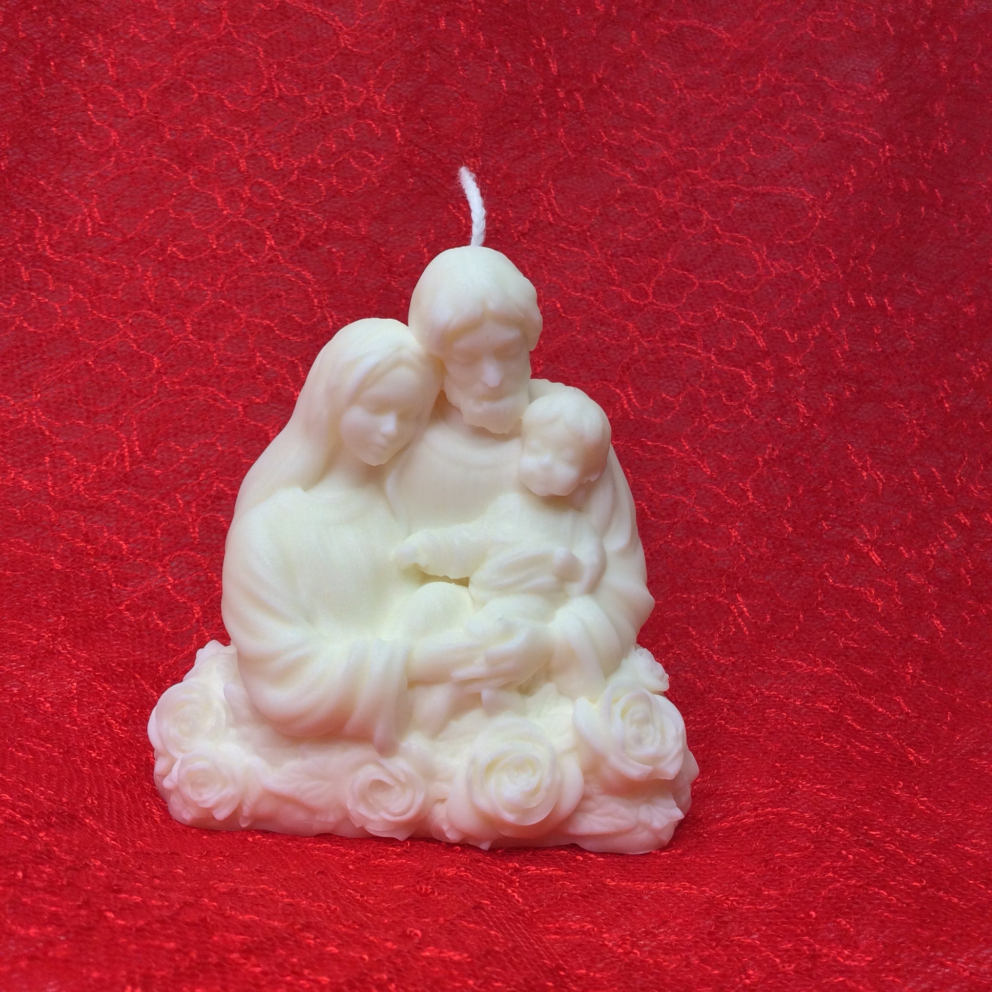 Vela artesanal de la Sagrada Familia con base de rosas sobre fondo blanco.
