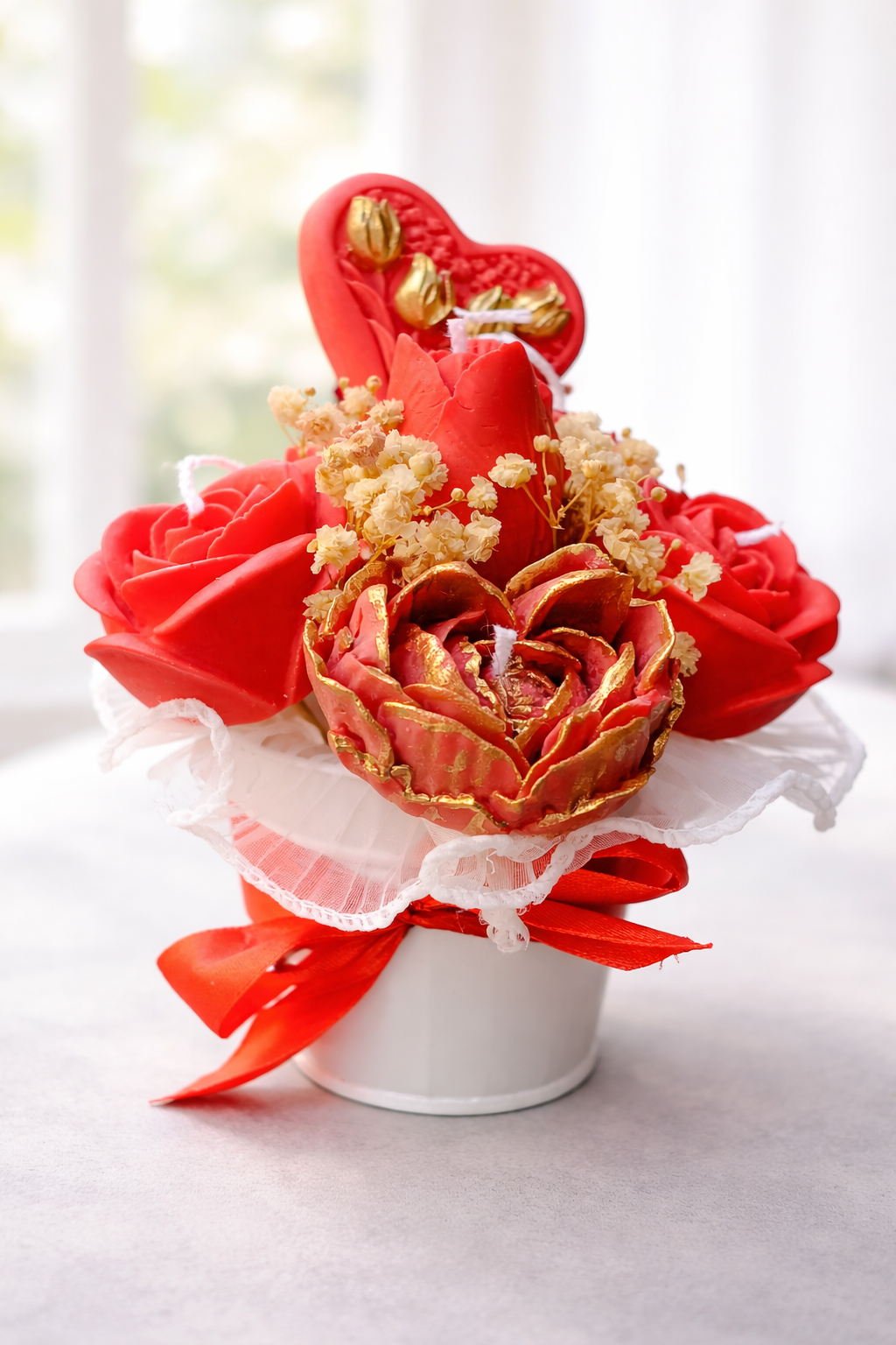 Arreglo floral de lujo “Llama Eterna” con rosas rojas artesanales y flor central ribeteada en dorado, decorado con delicadas flores secas color marfil, corazón ornamental rojo y base blanca con lazo satinado, iluminado por luz natural suave que resalta su elegancia romántica.