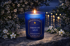 Vela aromática de lujo Jardín de Azur encendida entre flores blancas al atardecer, aroma floral sofisticado con inspiración mediterránea y atmósfera elegante.