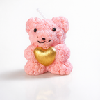Vela de diseño en forma de osito rosa empolvado con corazón dorado, pieza artesanal en cera natural, fotografía editorial premium de estilo delicado y romántico.