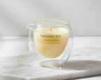 Vela de Masaje Kome to Sakura de NAGOMI, en vaso de cristal doble capa, sobre una elegante pieza de mármol blanco, con brillo y claridad mejorados.