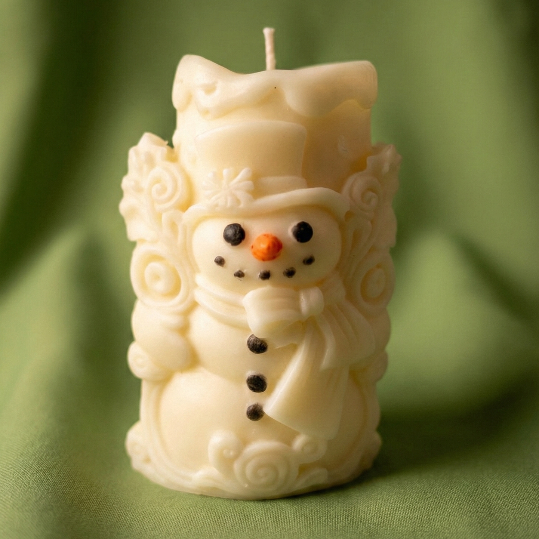 Vela decorativa navideña de cera color marfil tallada en forma de muñeco de nieve, con detalles pintados de ojos negros, nariz naranja, botones y un sombrero de copa y bufanda en relieve.