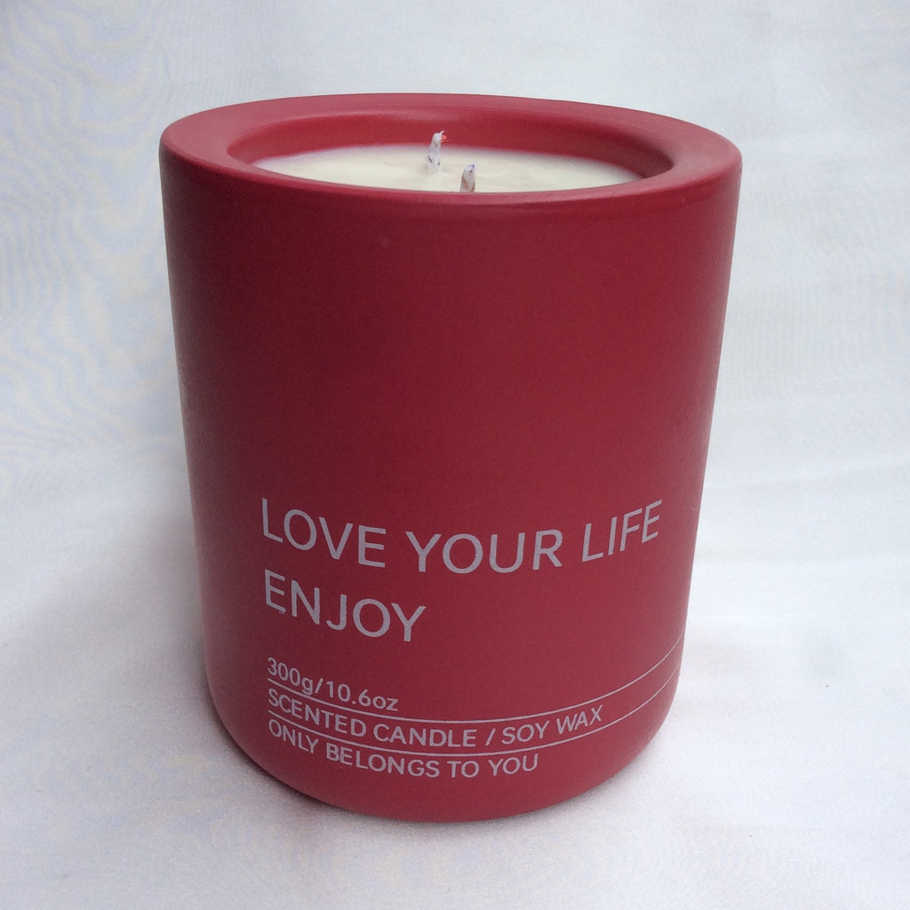 Primer plano de la vela aromática A Toda Vela BCN Rumbo al Alba en recipiente color rojo vibrante con la cera de soja blanca. Se lee "LOVE YOUR LIFE ENJOY" y "300g/10.6oz SCENTED CANDLE / SOY WAX". El envase resalta la cera vegetal ecológica y la doble mecha de algodón para una difusión óptima de la fragancia de Azahar y Bergamota.