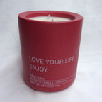 Primer plano de la vela aromática A Toda Vela BCN Rumbo al Alba en recipiente color rojo vibrante con la cera de soja blanca. Se lee "LOVE YOUR LIFE ENJOY" y "300g/10.6oz SCENTED CANDLE / SOY WAX". El envase resalta la cera vegetal ecológica y la doble mecha de algodón para una difusión óptima de la fragancia de Azahar y Bergamota.