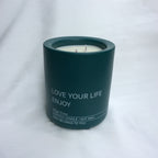 Vela perfumada Rumbo al Deseo Lujo verde oscuro de la colección "Una vela un rumbo". Contenedor con texto "LOVE YOUR LIFE ENJOY" y tres mechas.