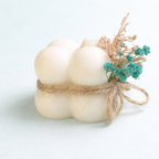 Vela artesanal de diseño en color azul pastel, decorada con flores secas naturales y lazo rústico, fotografía de estudio con estética suave, contemporánea y de lujo.