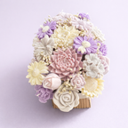 Centro floral artesanal en cera con flores en tonos lavanda, rosa empolvado y marfil, composición romántica para decoración de bodas elegantes.
