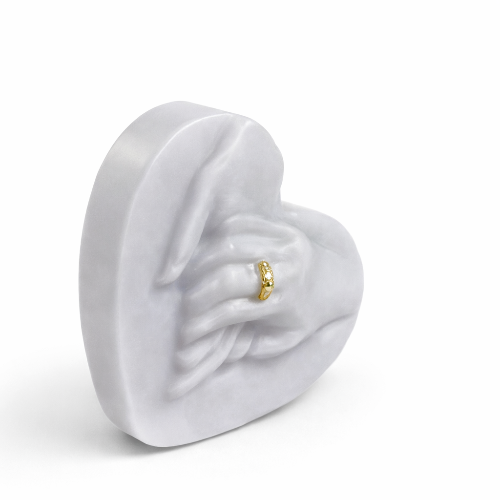 Vela escultórica corazón con manos unidas en tono gris perla, diseño contemporáneo en cera natural de alta calidad, detalle de anillo dorado integrado, pieza decorativa premium para interiores modernos y ambientes sofisticados.