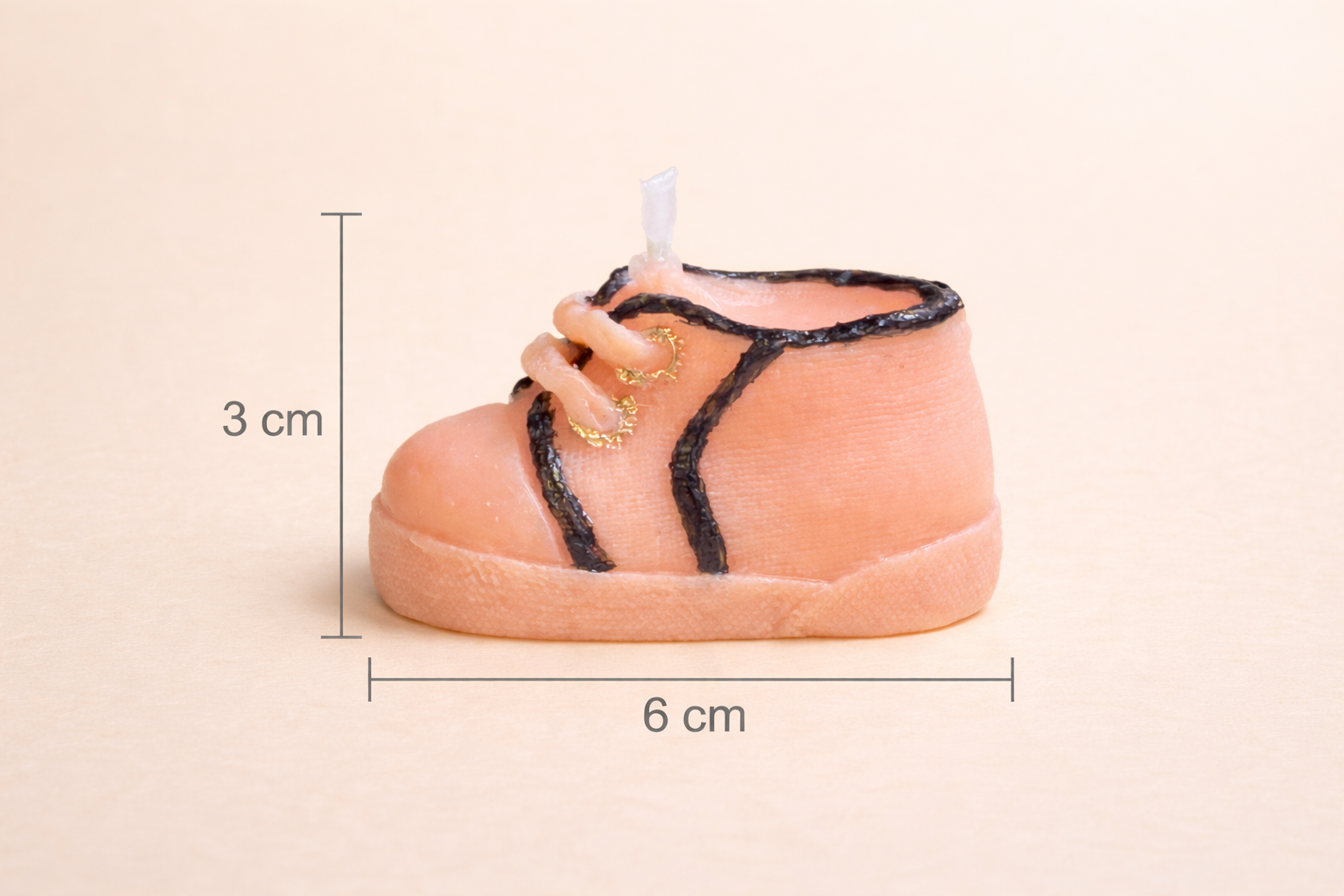 Vela decorativa artesanal en forma de zapatito de bebé color melocotón, dimensiones 3 cm de alto y 6 cm de ancho, fotografía de estudio minimalista para e-commerce de lujo.