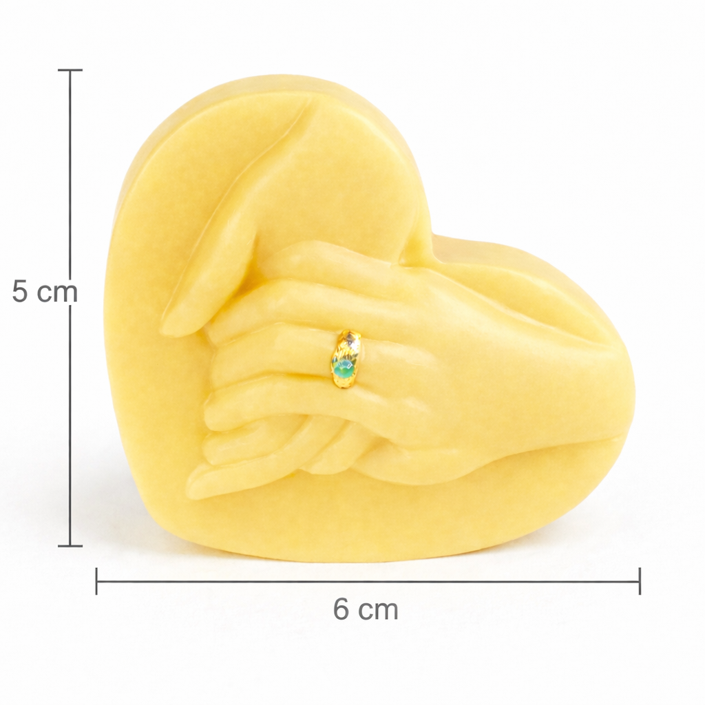Vela escultórica corazón con manos unidas de 5 cm de alto y 6 cm de ancho, elaborada en cera natural color amarillo suave, diseño minimalista con detalle dorado, pieza decorativa compacta y exclusiva para regalo premium.