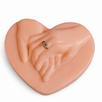 Vela artística en forma de corazón con manos entrelazadas color terracota nude, fabricada en cera natural con acabado satinado, diseño escultórico contemporáneo con anillo dorado, objeto decorativo de lujo para interiores cálidos y sofisticados.
