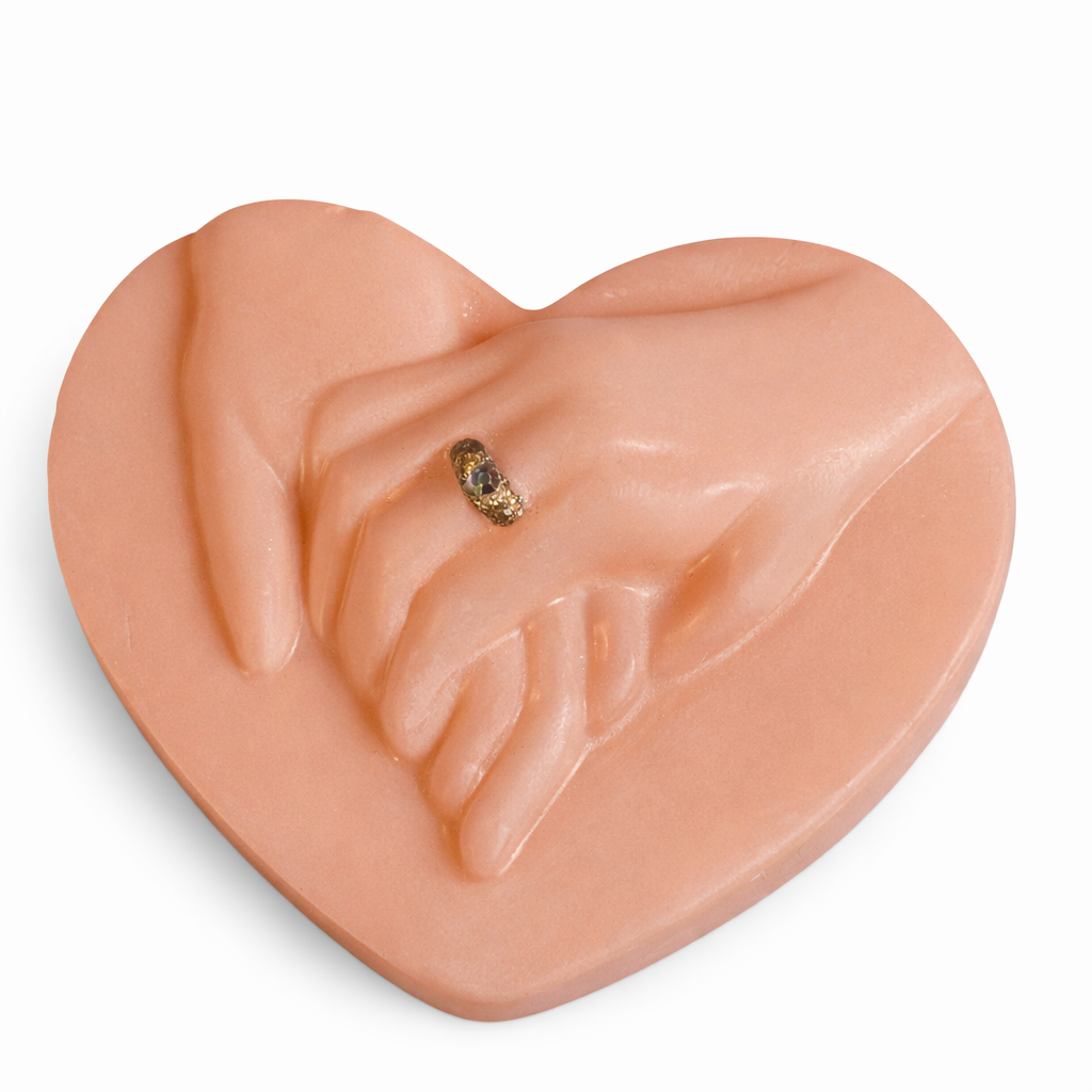Vela artística en forma de corazón con manos entrelazadas color terracota nude, fabricada en cera natural con acabado satinado, diseño escultórico contemporáneo con anillo dorado, objeto decorativo de lujo para interiores cálidos y sofisticados.