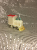 Vela de cumpleaños de tren artesanal con detalles pintados sobre fondo plateado.
