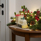 Vela de tren de Navidad decorando un centro de mesa festivo con pino, acebo y luces.