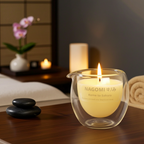 Vela de masaje Kome to Sakura colección Nagomi en vaso negro elegante con logo dorado, encendida en ambiente spa relajante.